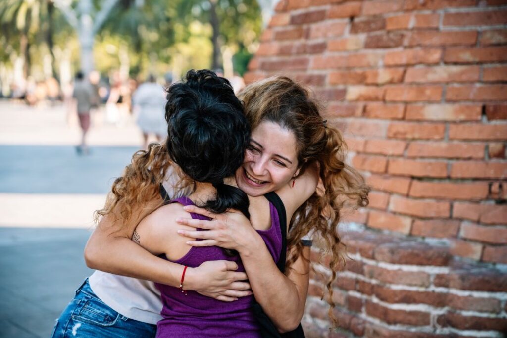 Two women hugging and smiling outdoors, representing friendship and community connection
